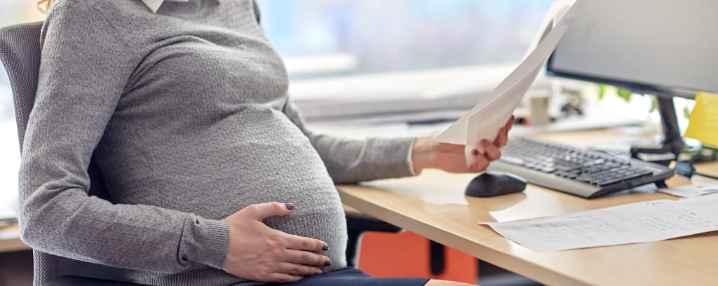 Photo of pregnant worker sitting at a desk and continuing to perform duties