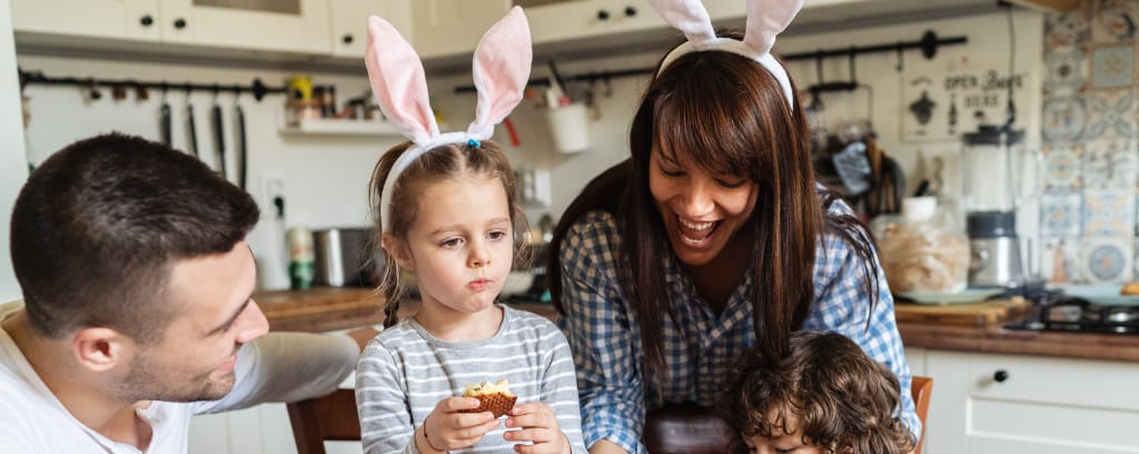 Photo of family celebrating Easter with rabbit ears on their heads. Child in foreground does not look happy.