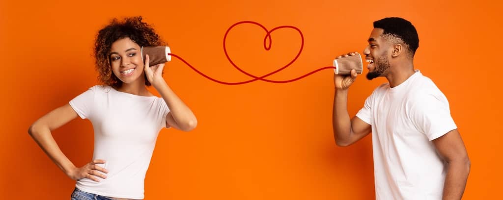 Photo of two people working well together by playing the telephone game in which they speak to each other through cans connected by a string that curls into a heart.