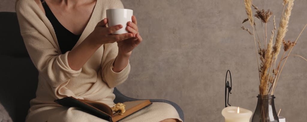 Photo of person cupping a mug with both hands while sitting with a journal in a peaceful setting