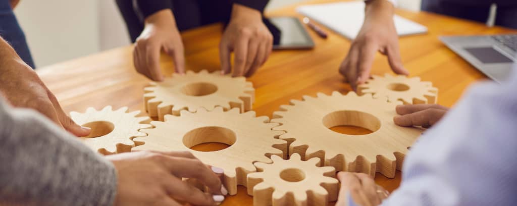 Photo of collaborators placing different sized wooden cogs together on a table.