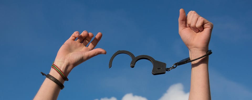 Photo of two hands in the air. One has been freed from a handcuff.