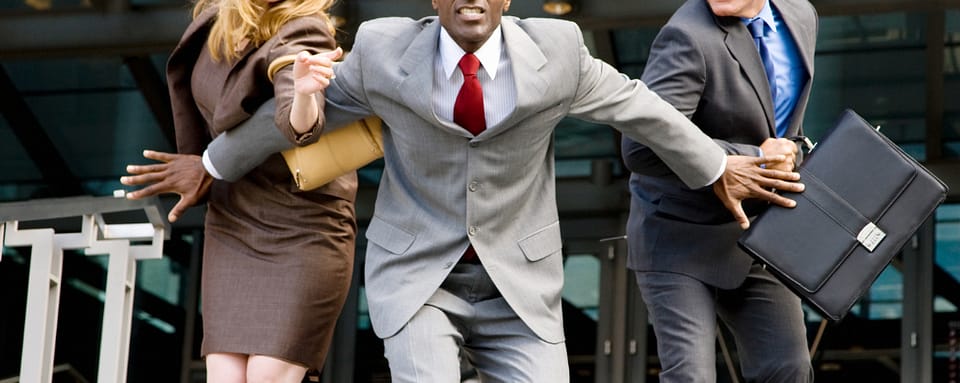 Photo of one person in a business suit holding two others back