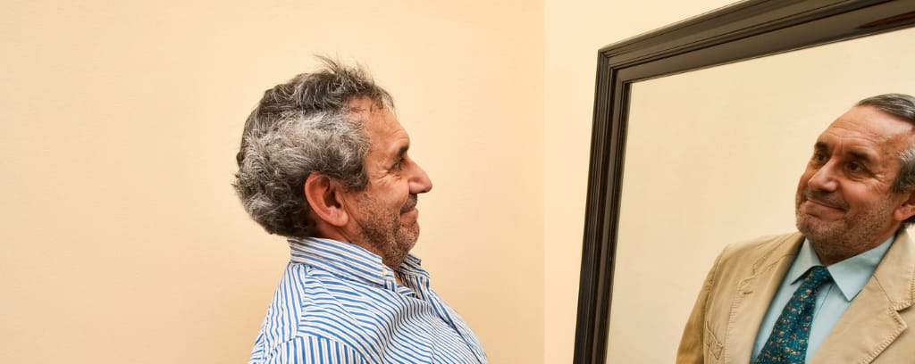Photo of man looking in mirror seeing a much more polished version of himself.