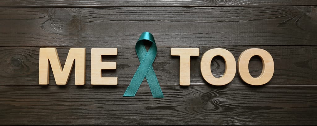 Photo of the words "Me Too" on a wood background with a teal ribbon.